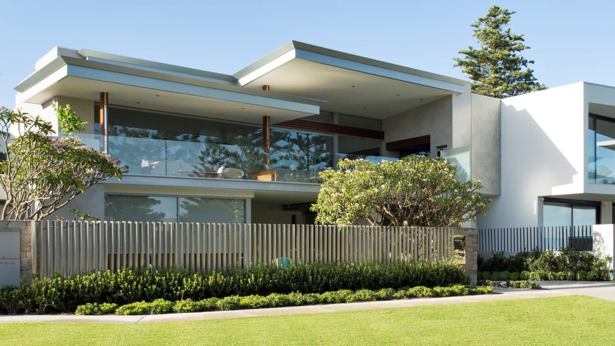 A beautiful modern concrete home with frangipanis and hedging.