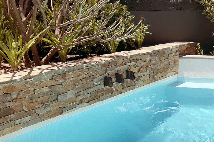 water features pouring into a pool through a stone wall.