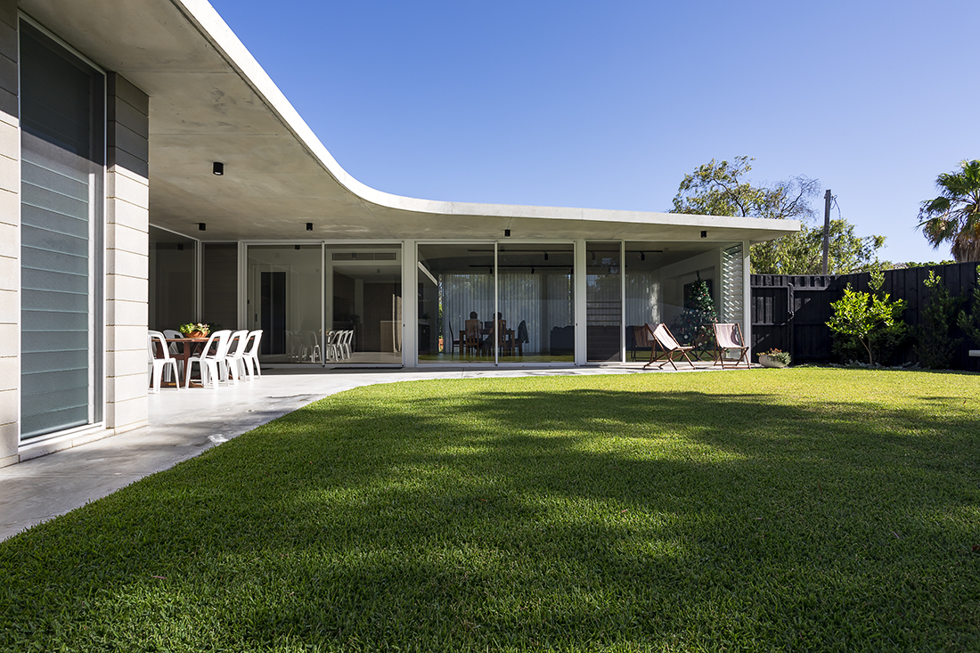 A mid-century style contemporary concrete home with a curved roof and thick green lawn