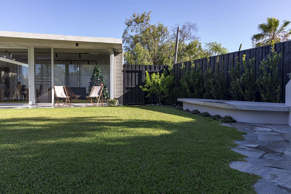 A backyard with thick green lawn and crazy paving.
